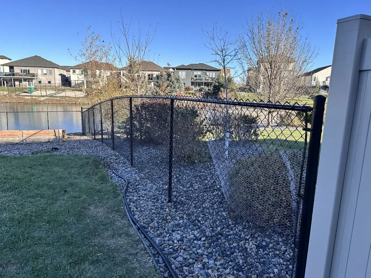 Black chain link fence curving smoothly along a sloped, landscaped yard