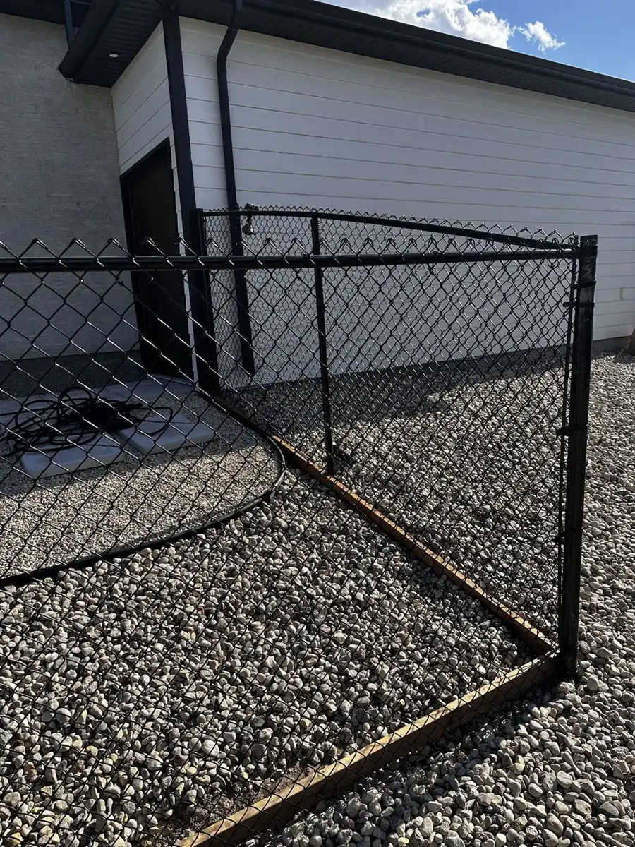 Wood running board along the bottom of a black chain link fence separating rock from landscaping